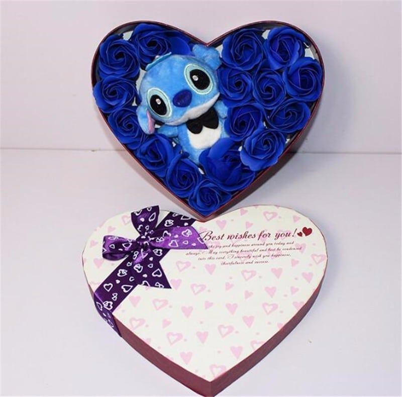Niebieska przytulanka Sticha znajduje się w pudełku w kształcie serca. Wokół niego znajdują się niebieskie róże. Na wieczku pudełka znajduje się fioletowa wstążka z napisami i motywami serca. Stich ma na sobie czarną muszkę.