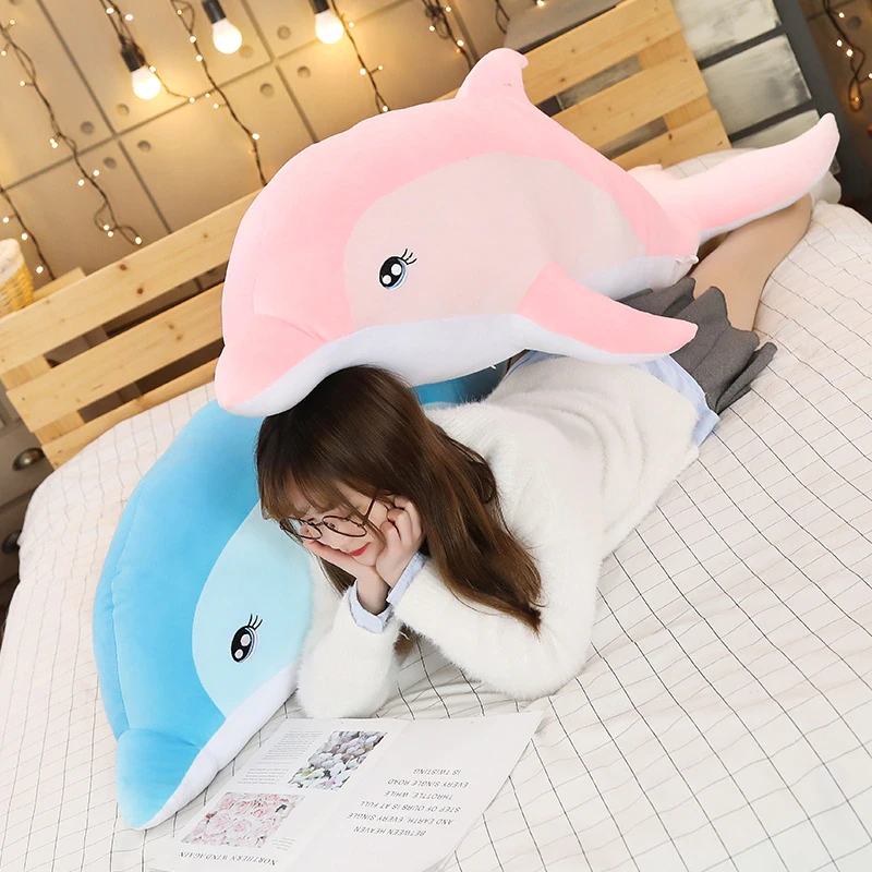 Przytulanka delfin dla dziewczynki na łóżku z dziewczynką na ręku