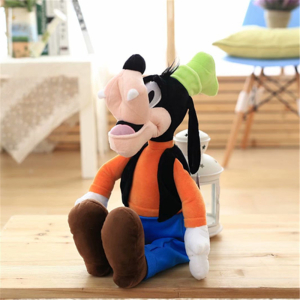 Pluszowa zabawka przedstawiająca głupkowatą postać Disneya siedzącą na parkiecie, ubraną w niebieskie spodnie i pomarańczowy top