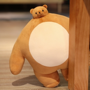 Pluszowa poduszka w kształcie brązowego niedźwiedzia z beżowym brzuchem przed nogą drewnianego mebla na drewnianej podłodze