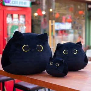 Trzy czarne pluszowe koty w trzech różnych rozmiarach. Ustawione na drewnianym stole.